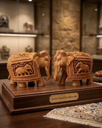 A pair of intricately hand-carved wooden Sikaar elephant figurines displayed on a polished wooden stand with a HandiCrush brass plaque