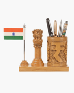 A wooden desk organizer set featuring a small Indian flag on a silver pole, a carved wooden pillar sculpture, and a matching carved cylindrical pen holder filled with pens, all mounted on a rectangular wooden base against a plain white background.