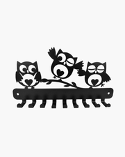 Black metal wall art featuring three stylized owls perched on a branch, shown against a plain light background.