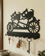 Close-up wall-mounted view of decorative black metal cats on bicycle key hanger with keys hanging on standard entryway wall.