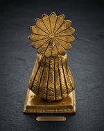 Back view of a HandiCrush golden brass traditional figurine featuring a sun-like decorative halo attached to a textured dress, resting on a square base with an 'Ancient Vestments' plaque against a dark slate background