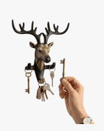 Hand placing key on deer wall key holder, decorative metal hook rack for organizing keys
