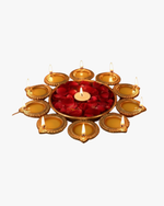 A circular arrangement of glowing golden diyas surrounding a bowl filled with red rose petals and a central candle, creating a warm festive decoration for Diwali. 🪔🌹✨