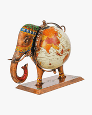 A handcrafted metal elephant figurine with a vintage world globe integrated into its body. The elephant is decorated with traditional Indian multi-colored hand-painted patterns and meenakari-style details on its head and legs. Set on a sturdy rectangular base