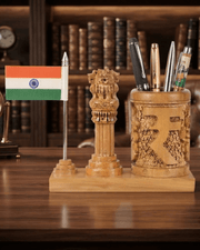 A carved wooden desk organizer set on a wooden table, featuring a small Indian flag on a silver stick, a carved lion capital pillar, and a carved cylindrical cup holding pens and pencils.