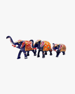 Tiered display of three blue metal elephants on a wooden pedestal with brass accents and green marble flooring