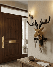 Decorative gold and black deer head key hanger mounted on a textured entryway wall next to a wooden door and bench