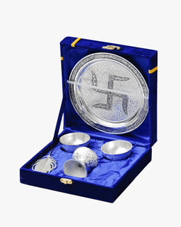 Open blue velvet gift box showing silver pooja thali set with diya bowls and feather spoon