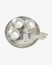 Top view of silver pooja thali set with diya bowls kalash and decorative spoon on engraved plate
