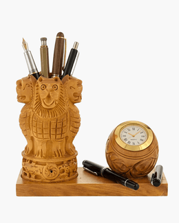 Carved wooden Ashok Stambh lion capital pen stand and round clock styled on a wooden office table with books and globe.